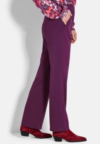 Lila weit geschnittene Hose aus weichem Stoff, mit Seitentaschen. Kombiniert mit roten Wildleder-Ankle Boots mit einem niedrigen Absatz und dekorativer Naht.