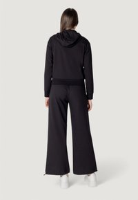 Felpa nera con cappuccio abbinata a pantaloni morbidi e a vestibilità rilassata. Presenta un cappuccio, polsini a coste e gambe dei pantaloni larghe.