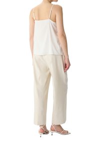 White silk camisole with thin straps paired with loose, cream-colored trousers. Outfit features minimalistic design and smooth texture.