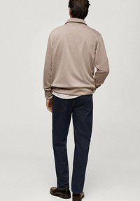 Felpa beige chiaro con colletto, indossata sopra una camicia bianca, abbinata a jeans blu scuro e scarpe marroni, vista da dietro.