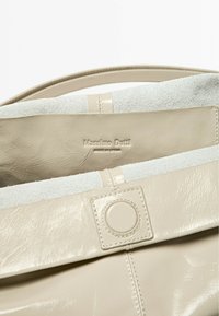 Beige leather bag with a smooth finish, featuring a suede lining, flat strap, and a button closure. Logo embossed on the interior.
