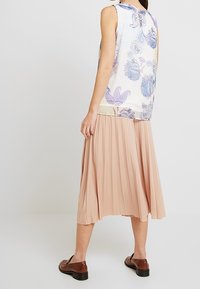Top senza maniche in tessuto leggero con motivi floreali blu; abbinato a una gonna a pieghe beige fino al ginocchio e scarpe marroni scure.
