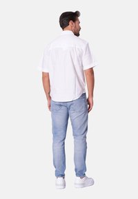 Camisa blanca de manga corta con dobladillo recto, combinada con vaqueros de color azul claro y zapatillas blancas, vista desde la parte de atrás. Diseño simple.