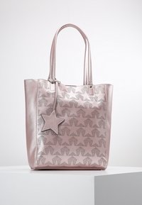 Metallisk rosa tygväska med stjärnmönster i perforeringar, dubbla handtag och en avtagbar stjärnformad charm. Slät yta och strukturerad form.