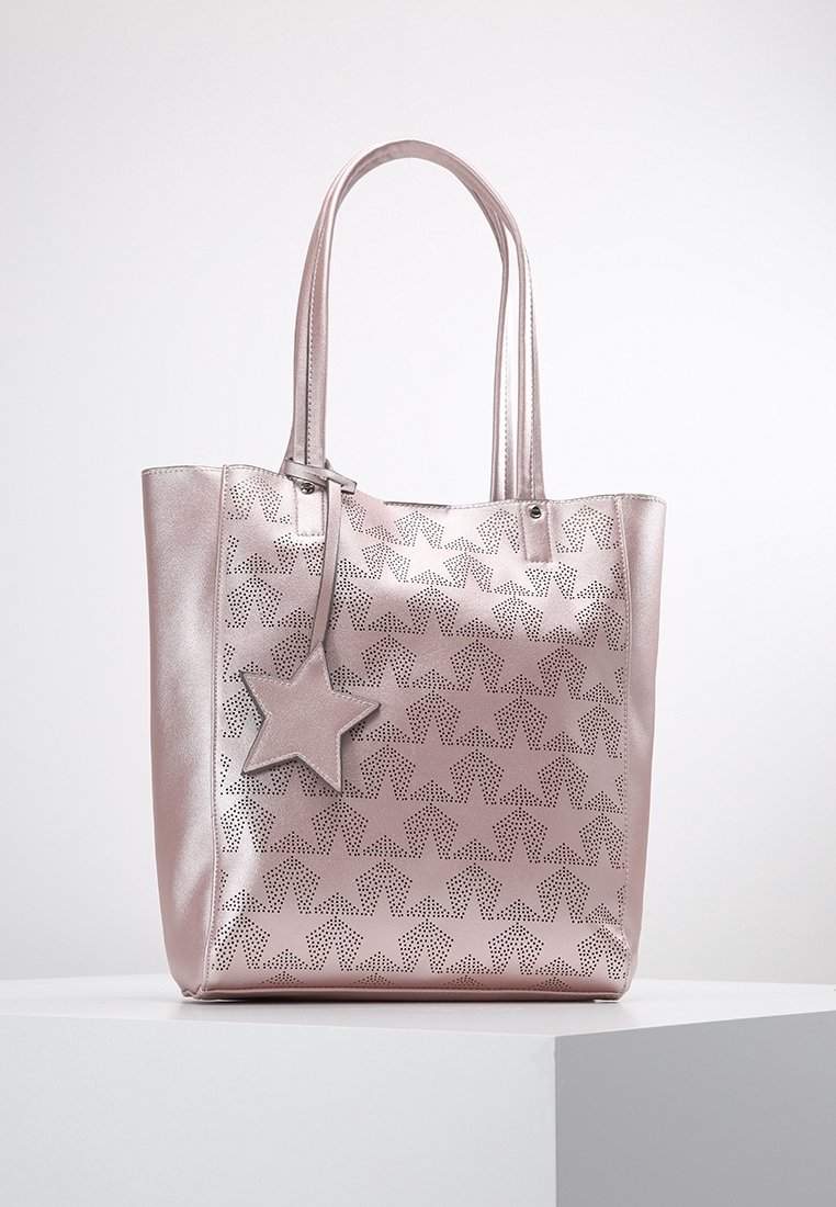 Metallisk rosa tygväska med stjärnmönster i perforeringar, dubbla handtag och en avtagbar stjärnformad charm. Slät yta och strukturerad form.
