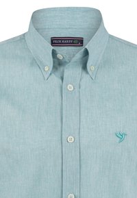 Camisa azul claro de botones en una tela texturizada, con un pequeño logo de ave bordado y botones blancos en la parte frontal.