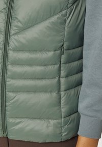 Lichtgroene donsbodywarmer met een doorgestikte textuur met horizontale naden, een ritssluiting aan de voorkant en een zijzak voor gemak.