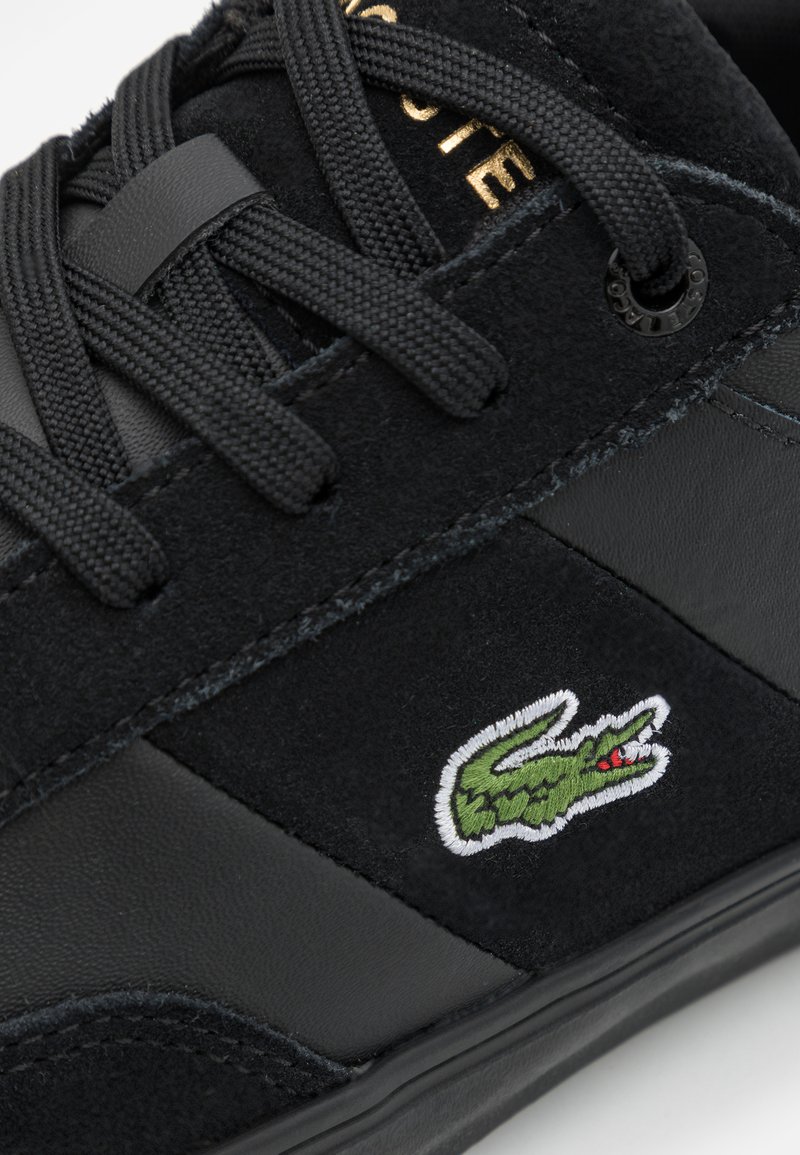 Czarna sneakersy z zamszu i skóry, z teksturowanymi czarnymi sznurówkami oraz zielonym i białym haftowanym logo krokodyla.