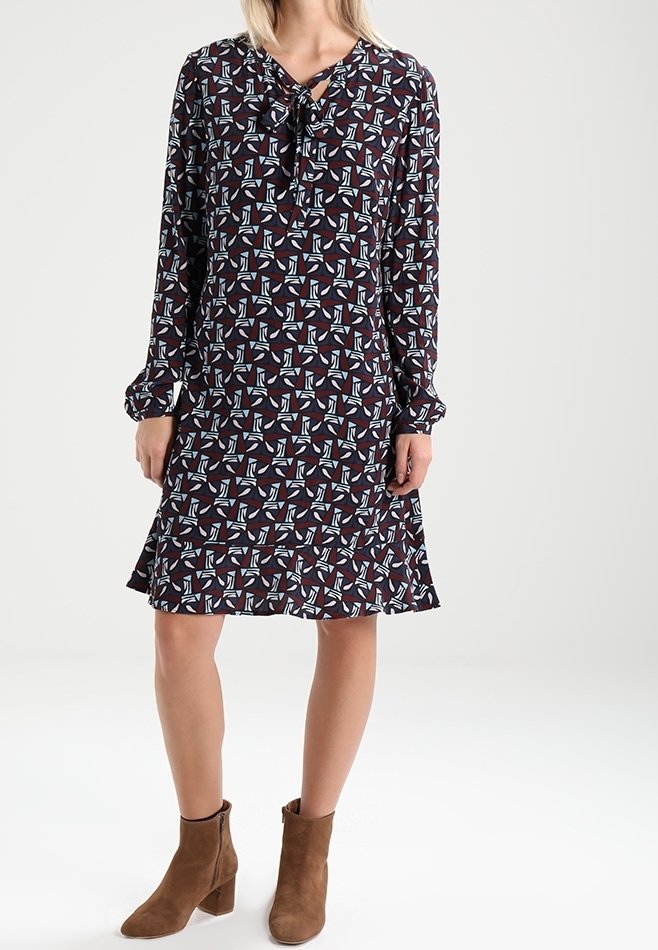 Robe à manches longues et longueur genoux de couleur bordeaux avec un motif géométrique de formes bleues et blanches ; dotée d'un col à nouer et d'un tissu doux.
