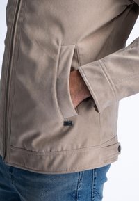 Beige faux suede jack met een ritssluiting aan de voorkant, schuine zijzakken en gestikte details. Bevat een klein merkje op de onderste zak.