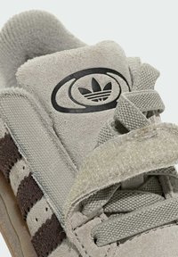 Gray suede Adidas sneaker with black three-stripe design, Velcro strap, woven laces, and Adidas trefoil logo on the tongue.