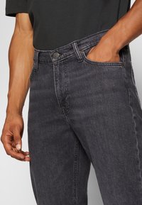 Dunkelgraue Denim-Jeans mit klassischem Fünf-Taschen-Design und Knopfleiste, mit einer leicht ausgewaschenen Textur für zusätzlichen visuellen Reiz.