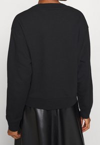 Sweat-shirt noir en tissu doux, avec un col rond, des épaules tombantes et une coupe décontractée, agrémenté de poignets et d'un ourlet côtelés.