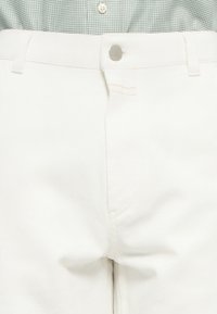 Pantalon en coton blanc avec une texture lisse, doté d'une fermeture éclair, d'un bouton argenté et de poches latérales. Pas de motifs visibles.