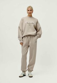 Beige oversized sweatshirt and matching joggers made of soft fabric. Text graphic on the front. Joggers feature elastic cuffs and side pockets.