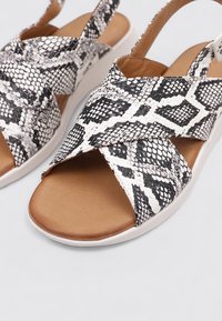 Sandales noires et blanches à motif peau de serpent avec des brides croisées, une semelle intérieure en cuir marron lisse et une semelle en caoutchouc blanche.