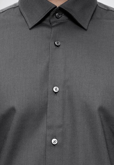Chemise gris foncé à boutons avec col pointu et texture à fines rayures diagonales, boutonnée au niveau du cou et de la poitrine.