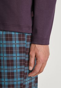 Haut mauve à manches longues avec un col rond, associé à un pantalon à carreaux marron et turquoise avec des lignes blanches en quadrillage et un léger éclat.
