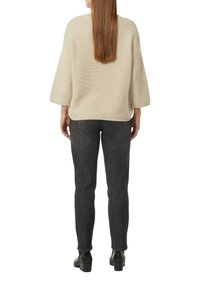 Cremefarbenem, strukturiertem Pullover mit weiten Ärmeln, kombiniert mit engen, dunklen Jeans und Stiefeletten, von hinten betrachtet.