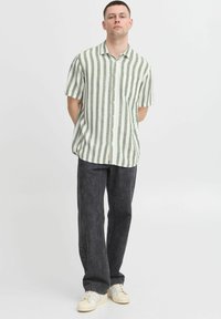 Krátký rukáv, zeleno-bílý pruhovaný shirt vyrobený z lehkého materiálu, spárovaný s tmavými, volně padnoucími džínami a bílými teniskami.