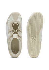 Zapatillas deportivas con un upper de ante y malla en color beige, cordones elásticos y una suela de goma texturizada con un detalle de logo.
