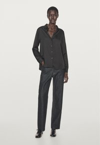 Czarna koszula z guzikami i kołnierzykiem, połączona z luźnymi ciemnymi dżinsami i czarnymi butami. Gładka tekstura materiału i swobodny krój.