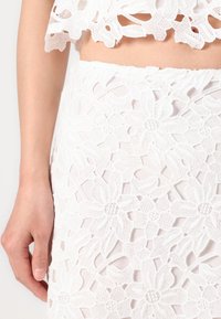Top alb brodat, cu un design din dantelă florală și detalii tăiate, asortat cu o fustă care prezintă un model floral similar și o textură corespunzătoare.