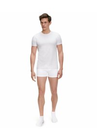 T-shirt bianco in cotone a maniche corte, abbinato a boxer bianchi. Il modello indossa calze alla caviglia bianche. Design semplice e aderente.