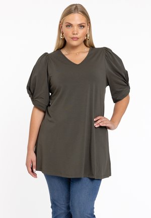 Olivgrünes V-Ausschnitt-Tunika mit Puffärmeln, aus weichem Stoff gefertigt. Der Saum fällt unter die Hüften und wird mit blauen Jeans kombiniert.