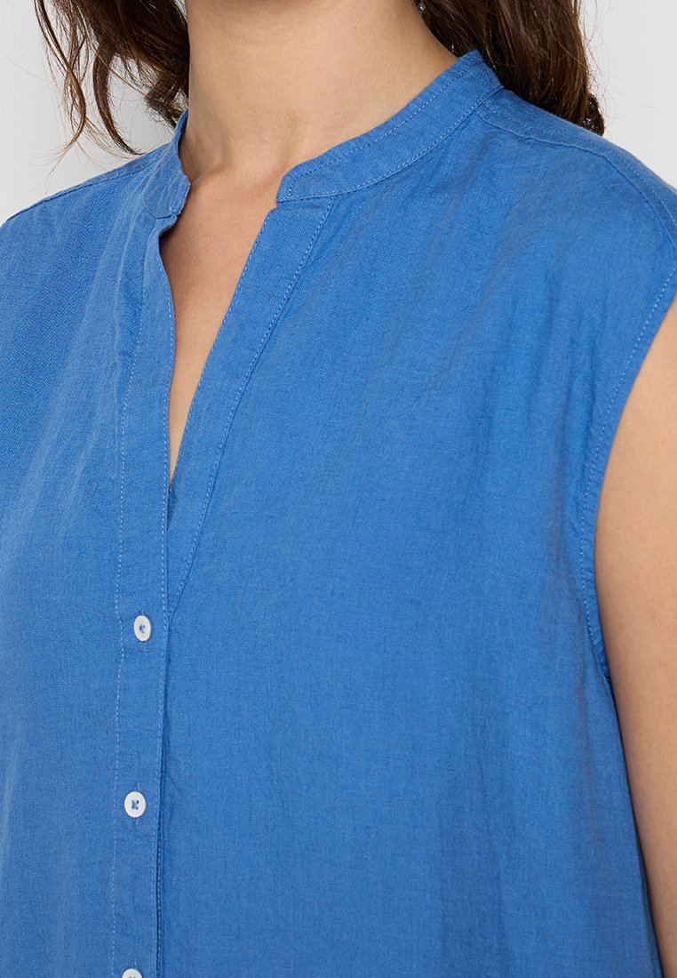 Niebieska koszula z krótkim rękawem, wykonana z lekkiego materiału, z kołnierzykiem i zapięciem na guziki. Gładka faktura, jednolity kolor bez wzorów.
