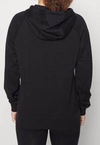 Sudadera negra con capucha y cordón, de mangas largas y puños acanalados. Textura suave con un bolsillo tipo canguro en la parte frontal, sin gráficos visibles.