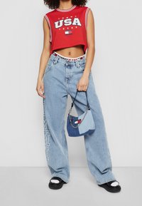 Top corto sin mangas rojo con gráfico "USA", jeans de pierna ancha azul claro y un bolso de patchwork azul con acento de cadena, sandalias de plataforma negras.