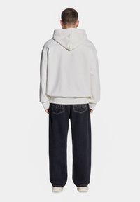 Biała bluza z kapturem o luźnym kroju, sparowana z ciemnymi dżinsami z kontrastowym przeszyciem i swobodną sylwetką.
