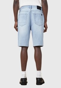 Shorts en denim bleu clair avec une coupe droite, dotés de deux poches arrière et de détails de couture, associés à des chaussettes blanches et des chaussures noires.
