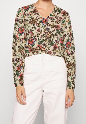Blusa a fantasia floreale in beige chiaro, con scollatura a V, maniche lunghe e polsini con bottone. Abbinata a pantaloni a vita alta di colore rosa chiaro.