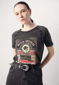 T-shirt nera in cotone con stampa grafica che presenta un motivo solare e del testo, maniche corte e una vestibilità rilassata, abbinata a jeans neri a vita alta e una cintura.