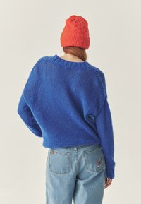 Niebieski sweter z dzianiny o luźnym kroju i prążkowanym dekolcie, w zestawie z jasnoniebieskimi dżinsami z czerwonymi haftami kwiatowymi na kieszeni.