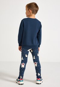 Marineblå sweatshirt med lange ærmer parret med leggings, der har polarbjørne, træer og sneprikker i et blødt, strækbart stof. Flerfarvede sneakers.