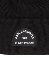 Gorro de punto negro con una etiqueta de logo y parte superior redondeada. La etiqueta tiene texto blanco sobre un fondo negro. Textura suave, diseño acanalado.
