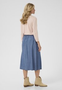 Svijetloružičasti top dugih rukava u kombinaciji s plavim traper suknjom do gležnjeva. Outfit upotpunjen bež čizmama do gležnjeva. Jednostavan i ležeran dizajn.