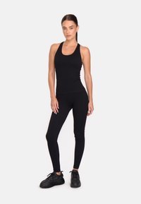 Musta urheilullinen tankkitoppi ja legginsit, jotka on valmistettu joustavasta kankaasta. Asusteessa on istuva muotoilu ja teksturoituja yksityiskohtia, ja se on yhdistetty mustiin lenkkareihin.