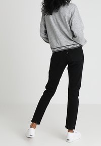 Felpa grigia con fascia in vita nera con logo Levi's, jeans neri e sneakers bianche. Capelli ricci visibili da dietro.