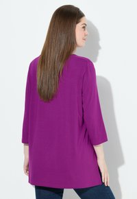 Violetti pitkähihainen tunika, jossa on rento leikkaus. Materiaali on sileä, ja suunnittelussa on pyöreä pääntie sekä puolipitkät hihat.