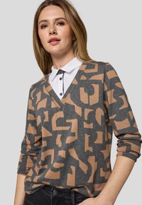 Grauer Strickpullover mit einem braunen abstrakten Muster, V-Ausschnitt-Design und Dreiviertelärmeln, getragen über einem weißen Hemd mit Kragen.