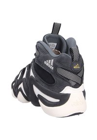 Schwarzer und grauer Sportschuh mit strukturiertem Obermaterial, auffälliger weißer Außensohle, Netzakzenten und markantem Adidas-Branding an der Ferse.