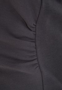 Gros plan d’un tissu gris foncé avec des coutures fronçant créant une texture froncée le long d’une couture verticale.