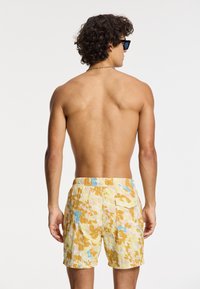 Shorts de bain avec un motif abstrait jaune, bleu et blanc, dotés d'une taille élastique et d'une poche arrière. Tissu texturé, longueur mi-cuisses.
