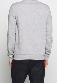Sudadera gris con mangas largas, cuello y dobladillo acanalados, hecha de una tela suave. Llevada con pantalones negros de rayas.
