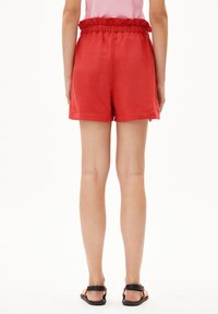 Shorts rouges à taille élastique fabriqués dans un tissu léger, présentant un design simple et une coupe décontractée, associés à des sandales noires.