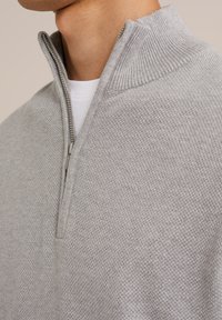 Grauer Strickpullover mit einem Viertelreißverschluss, der ein strukturiertes Muster und einen gerippten Kragen hat. Die innere Schicht ist weiß.